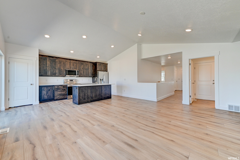 Kitchen with light hardwood / wood-style floors, lofted ceiling, stainless steel appliances, and an island with sink