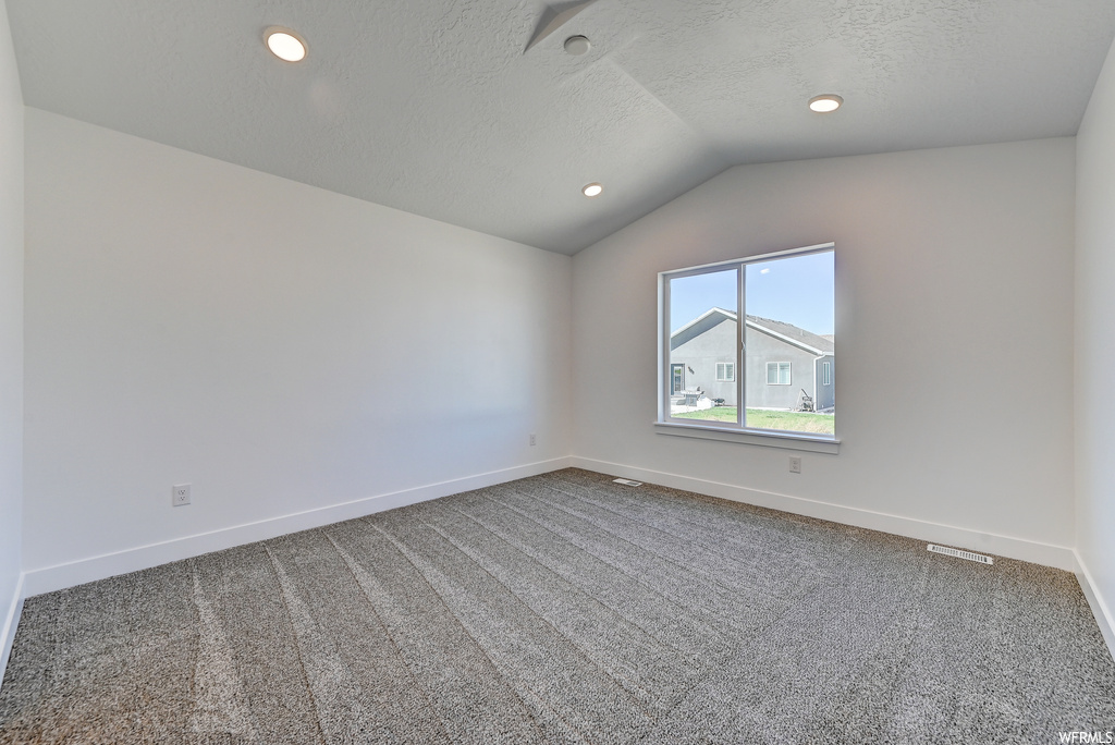 Empty room with vaulted ceiling, a textured ceiling, and carpet floors