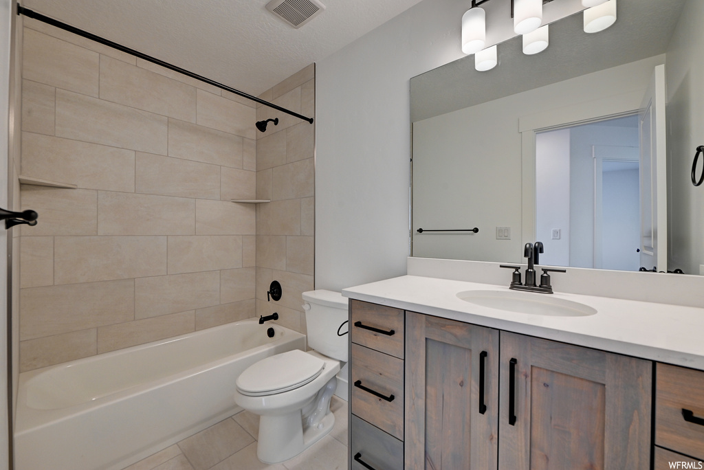 Full bathroom with tile flooring, toilet, vanity, a textured ceiling, and tiled shower / bath combo