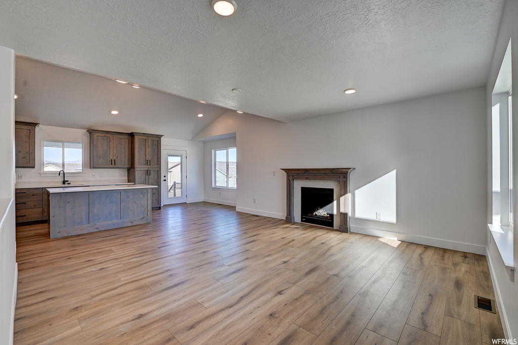 Unfurnished living room with lofted ceiling, a fireplace, a healthy amount of sunlight, and light hardwood flooring