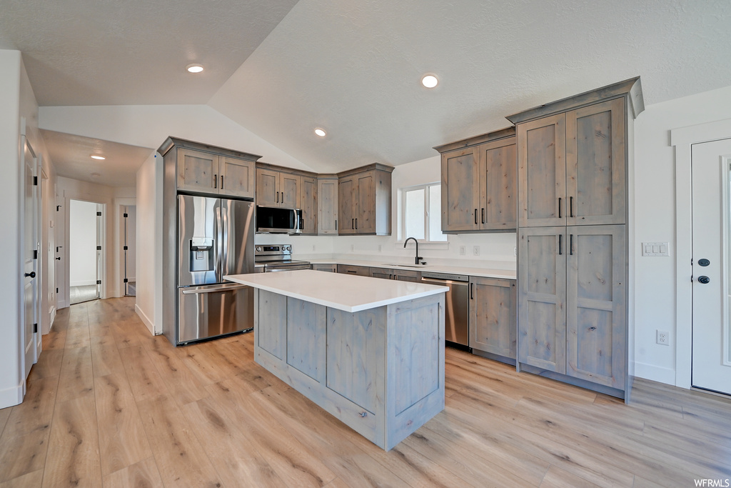 Kitchen with sink, vaulted ceiling, a center island, light hardwood flooring, and stainless steel appliances