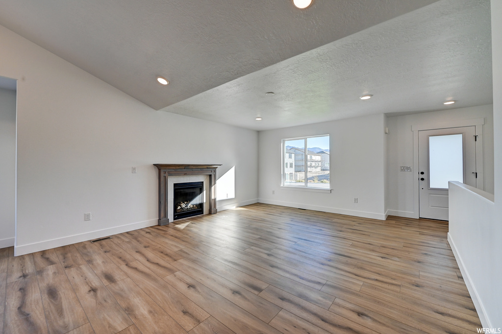 Unfurnished living room featuring a textured ceiling, light hardwood floors, and a fireplace