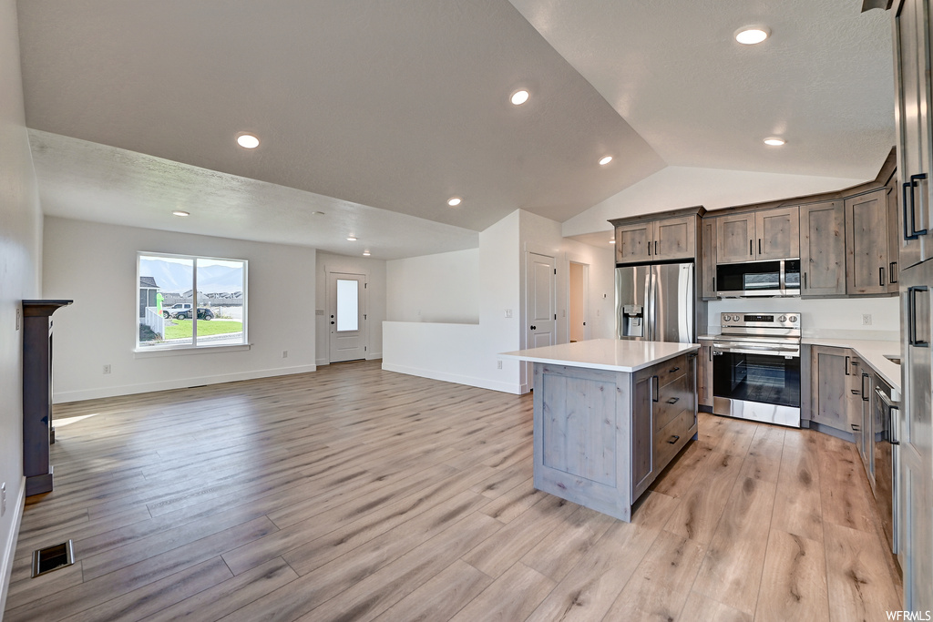 Kitchen featuring a center island, a fireplace, light hardwood floors, lofted ceiling, and stainless steel appliances