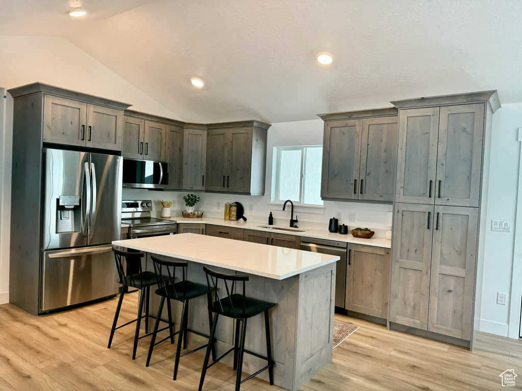 Kitchen featuring a kitchen island, lofted ceiling, appliances with stainless steel finishes, light hardwood / wood-style flooring, and sink