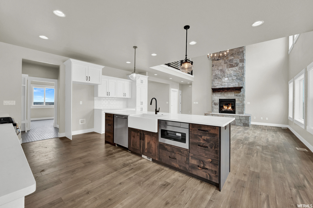 Kitchen featuring a fireplace, natural light, stainless steel dishwasher, pendant lighting, light countertops, and light hardwood flooring