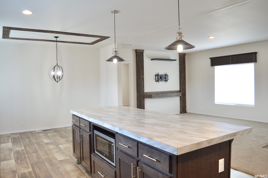 Kitchen featuring dark brown cabinets, hanging light fixtures, light carpet, light countertops, and stainless steel microwave