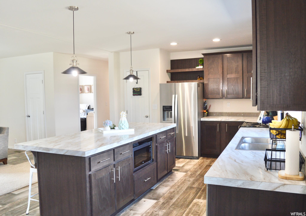 Kitchen with a kitchen bar, a center island, microwave, refrigerator, light countertops, pendant lighting, dark brown cabinets, and light hardwood floors