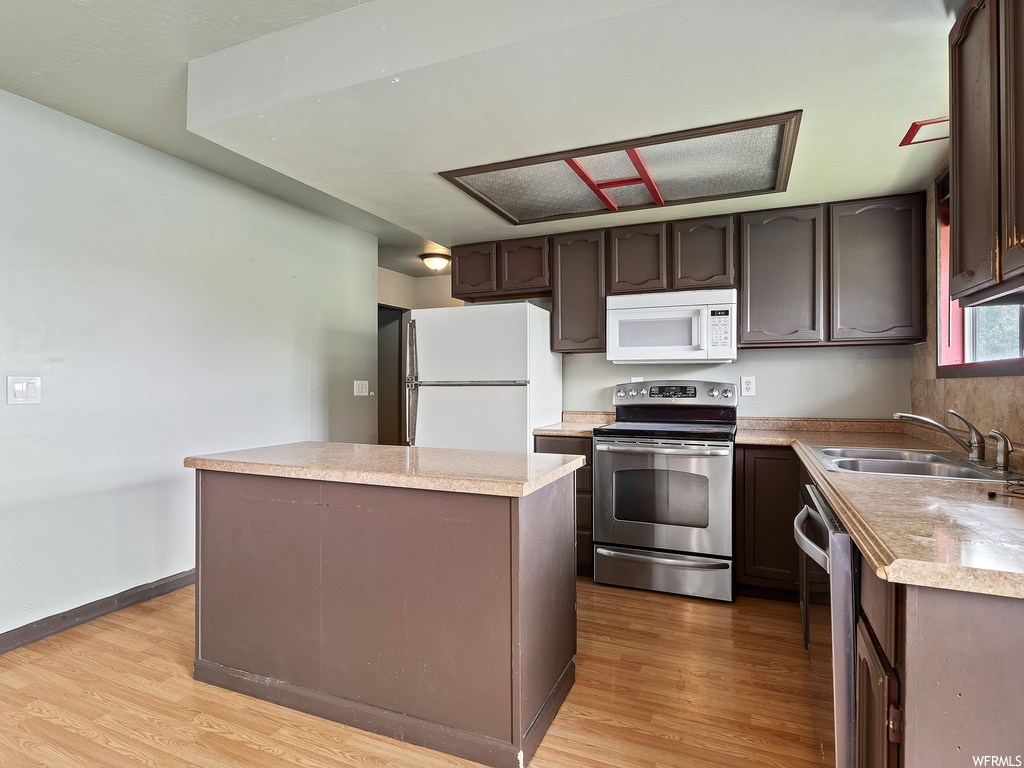 Kitchen with microwave, dishwasher, refrigerator, range oven, dark brown cabinetry, light countertops, and light parquet floors