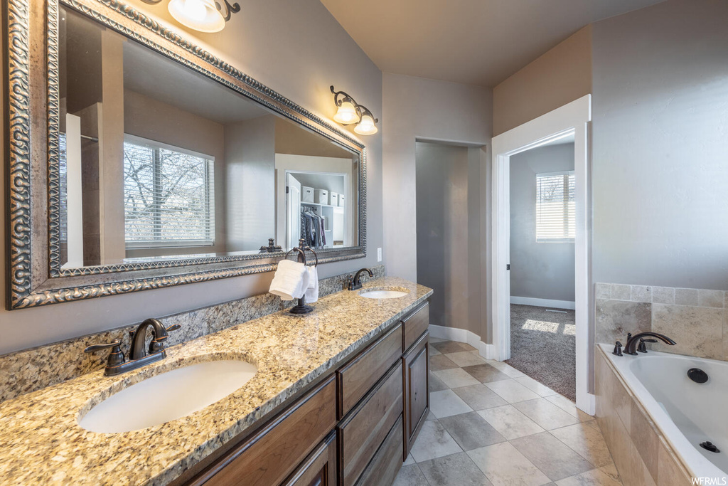 Bathroom featuring tile floors, natural light, double vanity, a bath, and mirror