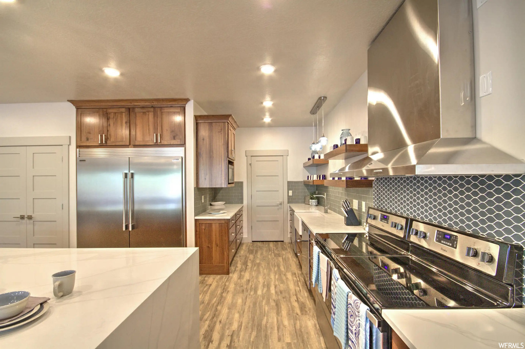 Kitchen with stainless steel refrigerator, range hood, and light hardwood floors