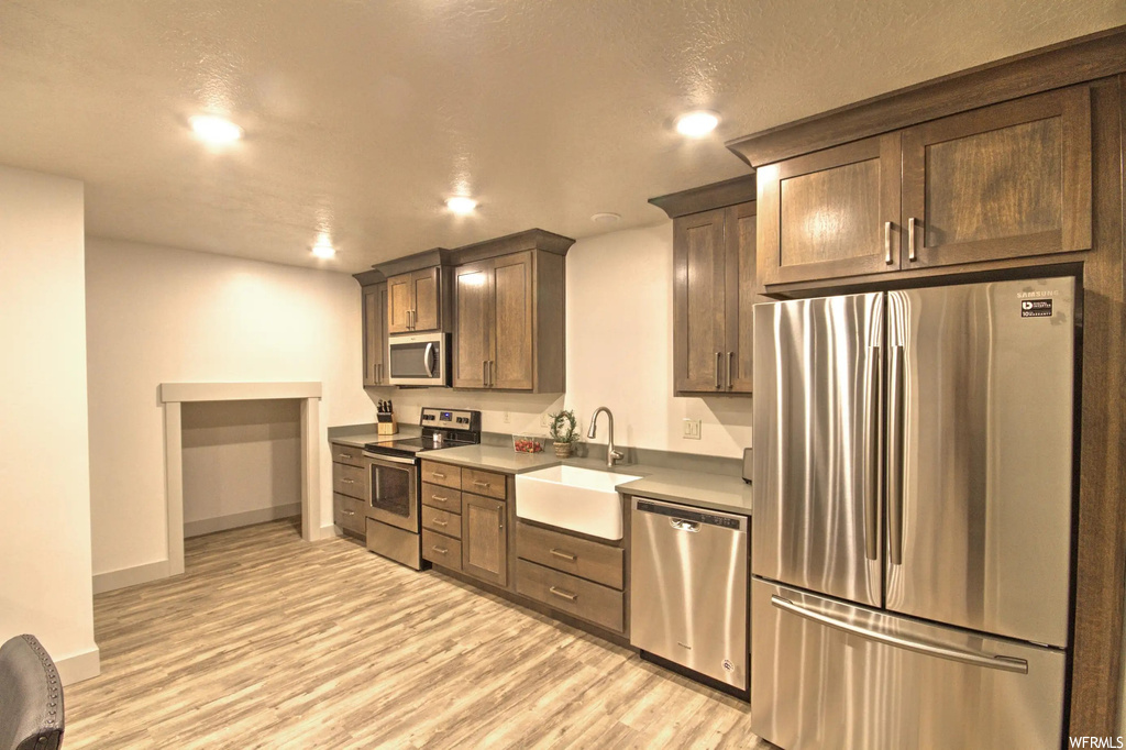 Kitchen featuring stainless steel dishwasher, microwave, electric range oven, refrigerator, brown cabinetry, and light flooring