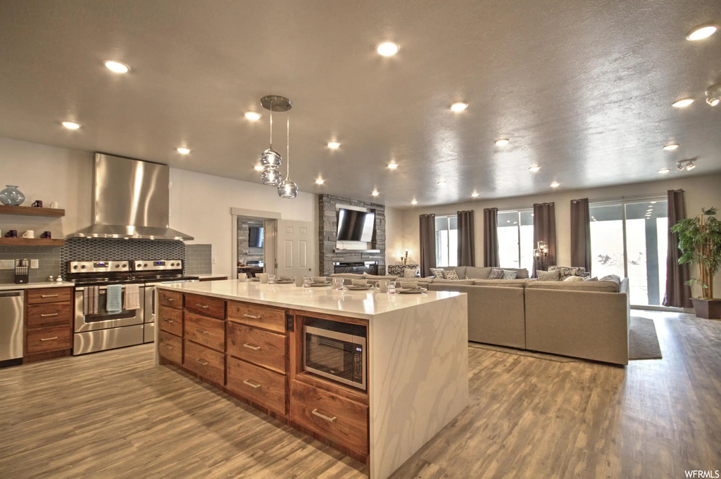 Kitchen featuring a wealth of natural light, stainless steel dishwasher, fume extractor, TV, microwave, range oven, pendant lighting, light countertops, and light hardwood flooring