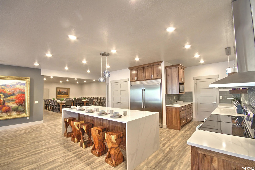 Kitchen with a kitchen breakfast bar, stainless steel refrigerator, range hood, pendant lighting, light countertops, and light parquet floors
