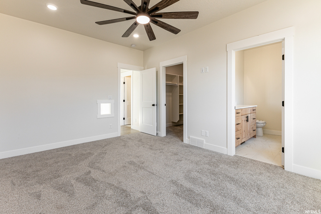 Unfurnished bedroom with light carpet, a spacious closet, ensuite bath, a closet, and ceiling fan