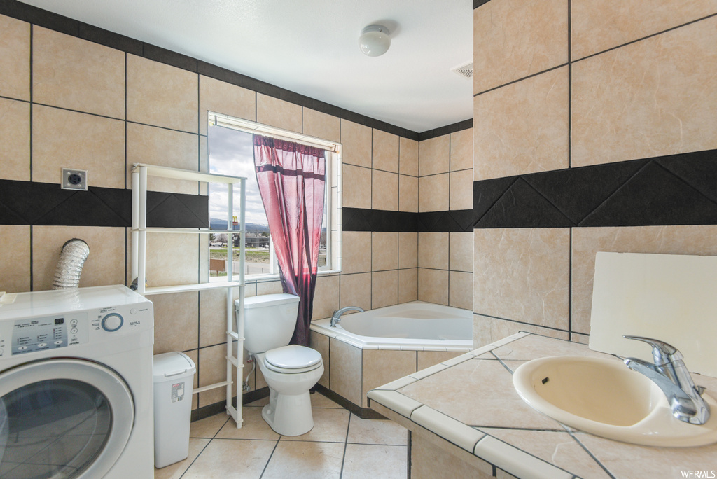 Bathroom with tile flooring, washer / dryer, toilet, sink, and a bathing tub