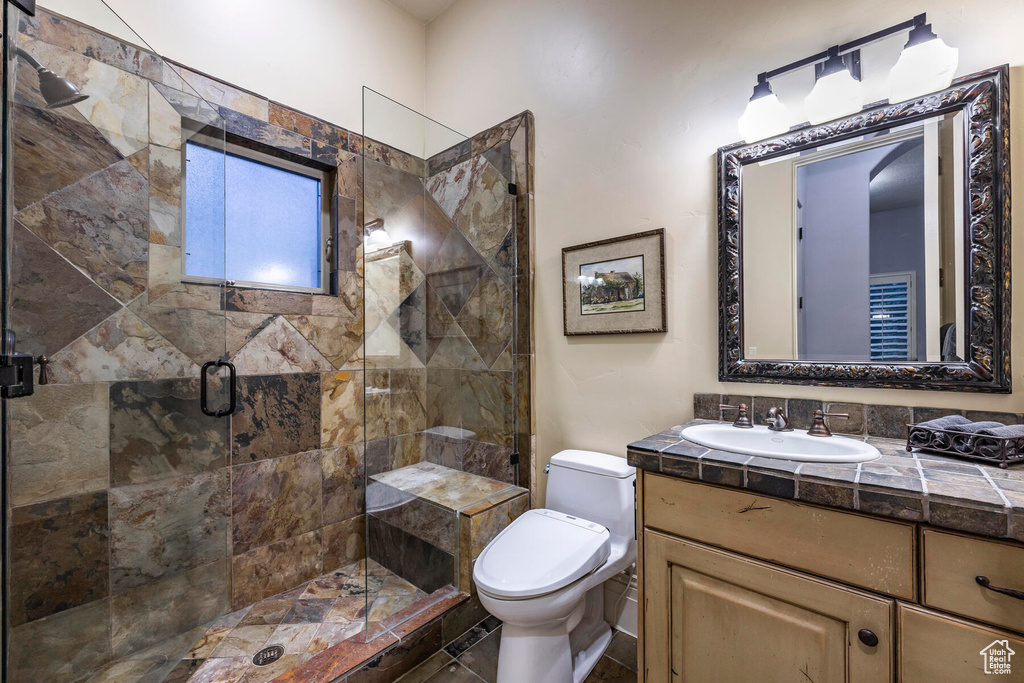 Bathroom featuring a shower with door, tile floors, large vanity, and toilet