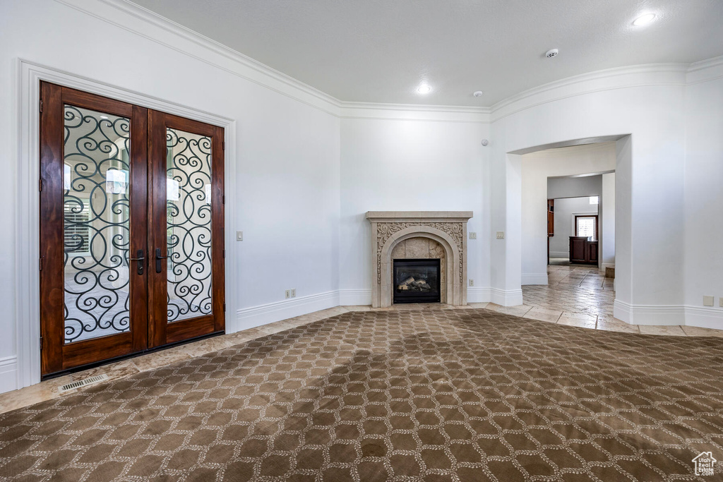 Unfurnished living room featuring a tile fireplace, dark tile floors, ornamental molding, and french doors