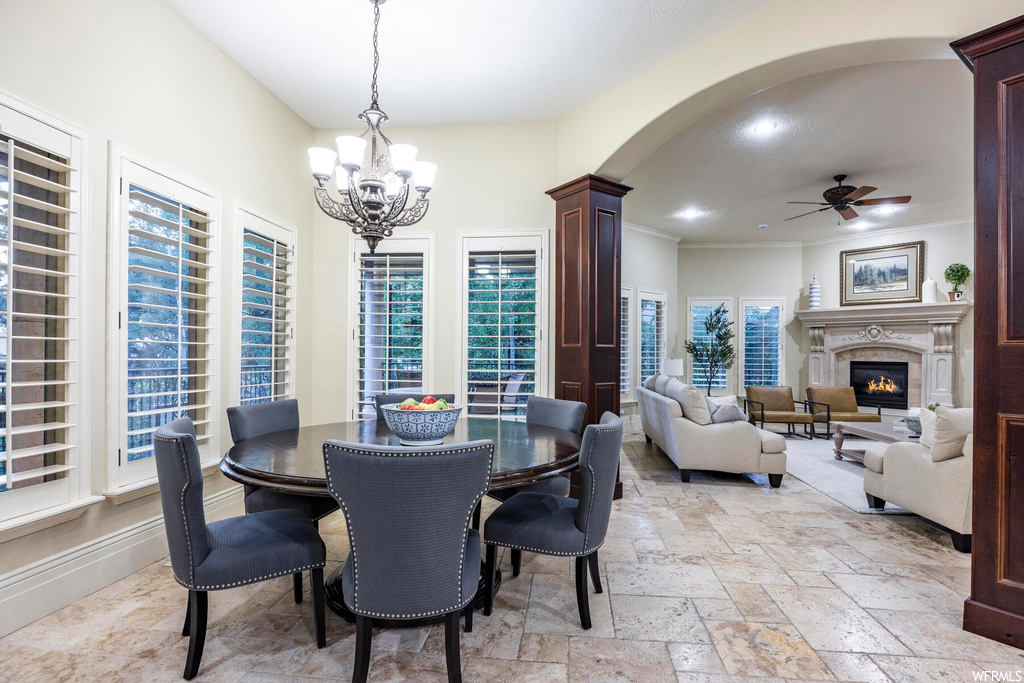 Dining space with light tile floors, ornate columns, crown molding, and ceiling fan with notable chandelier