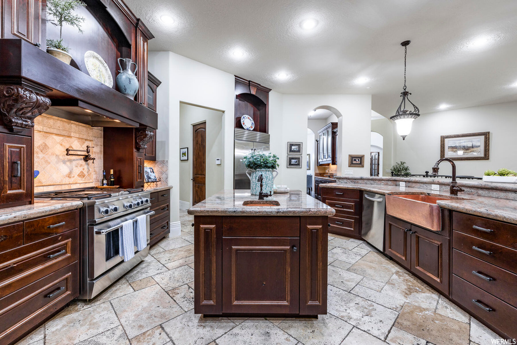 Kitchen featuring premium appliances, sink, pendant lighting, light stone countertops, and backsplash