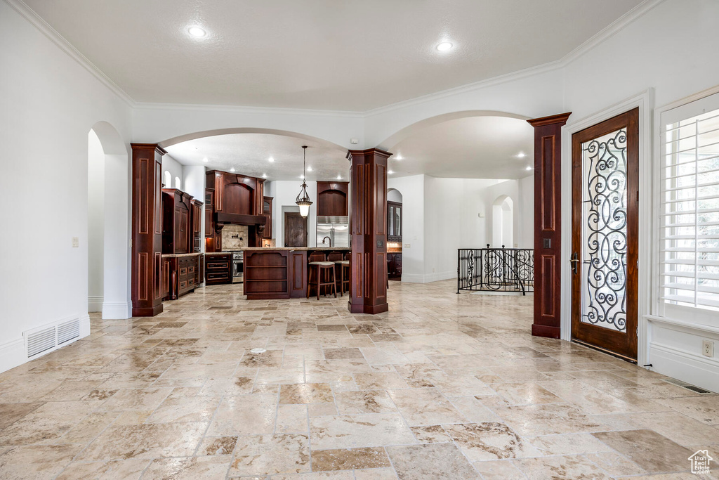 Entrance foyer featuring decorative columns, light tile floors, and crown molding