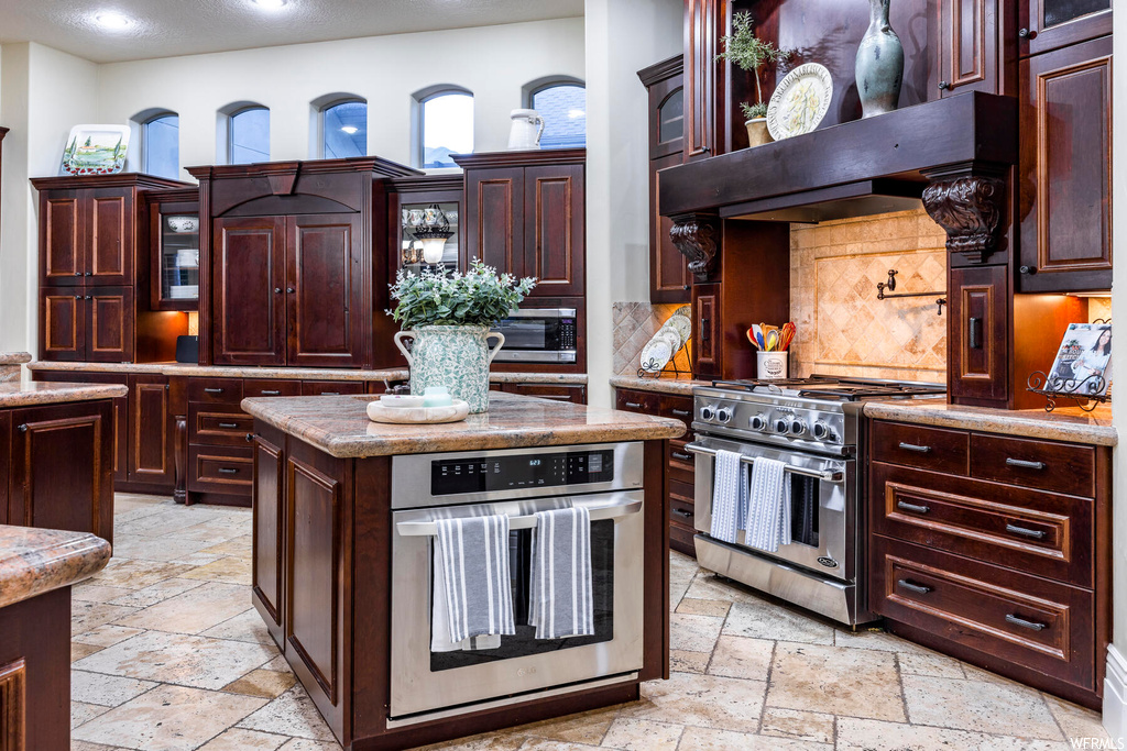 Kitchen featuring a center island, light stone countertops, tasteful backsplash, stainless steel appliances, and light tile floors