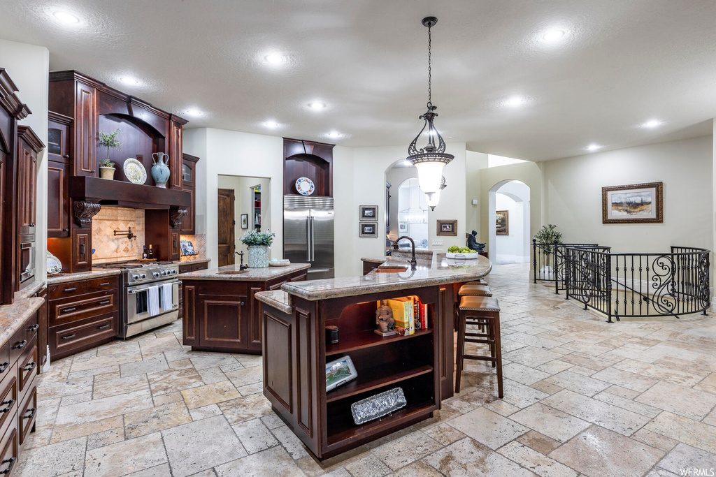 Kitchen featuring light tile floors, a kitchen island with sink, hanging light fixtures, a kitchen breakfast bar, and premium appliances