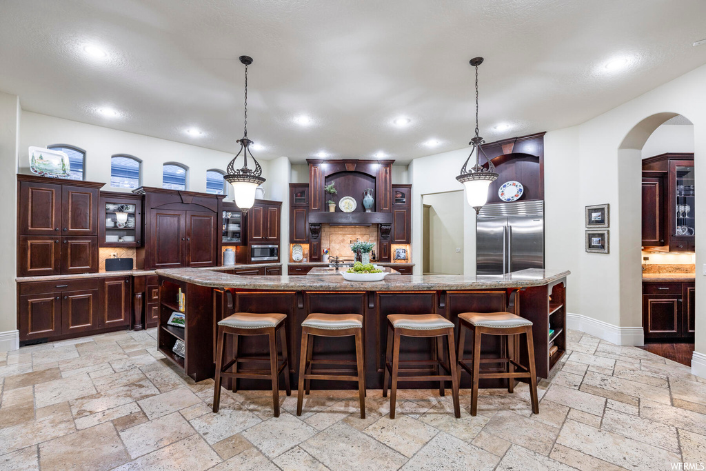 Kitchen with light tile flooring, built in appliances, decorative light fixtures, and a large island with sink
