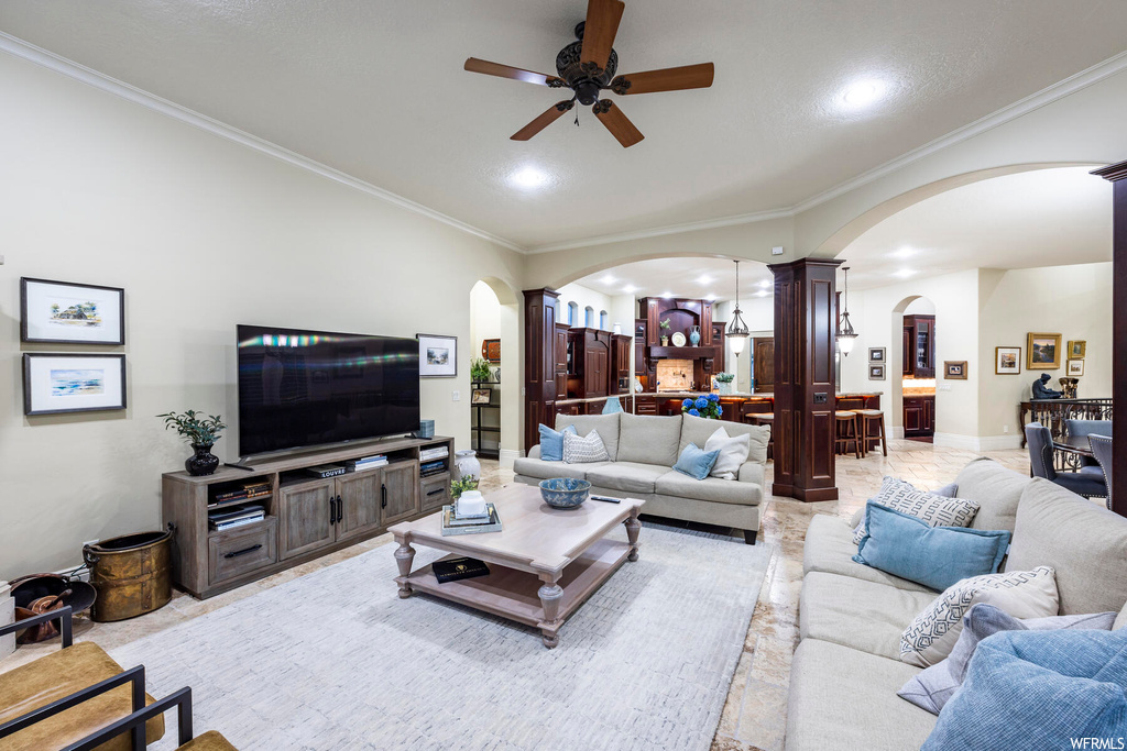 Living room featuring ceiling fan, decorative columns, light tile floors, and crown molding