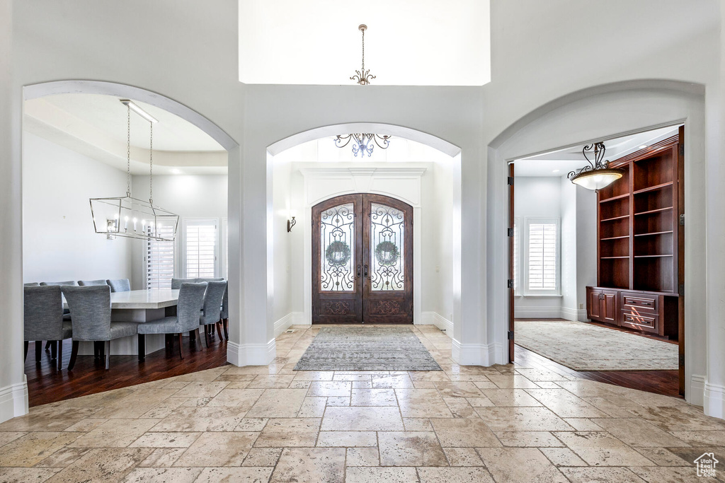 Tiled foyer entrance with a raised ceiling, a chandelier, french doors, and a high ceiling