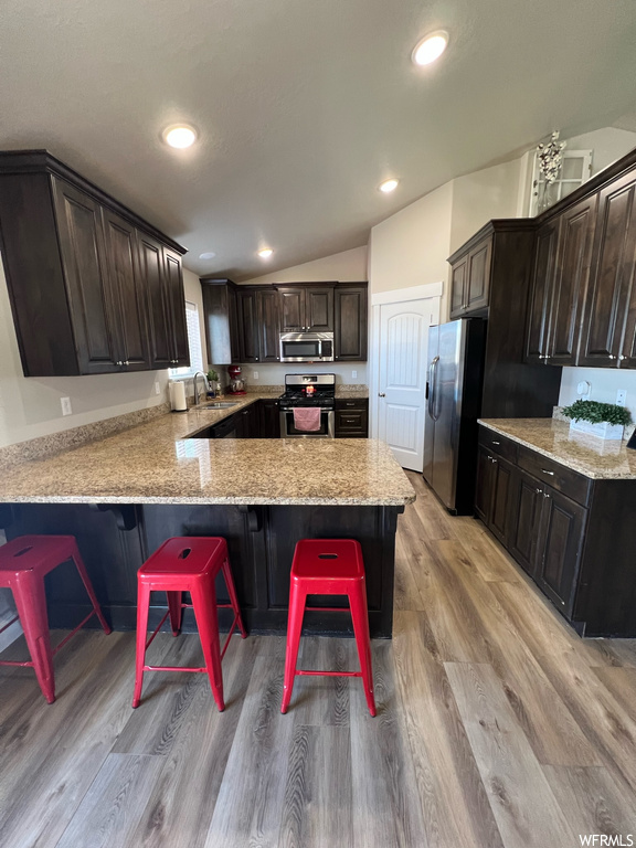 Kitchen featuring a breakfast bar area, microwave, range oven, stainless steel refrigerator, light hardwood floors, dark brown cabinets, and light stone countertops