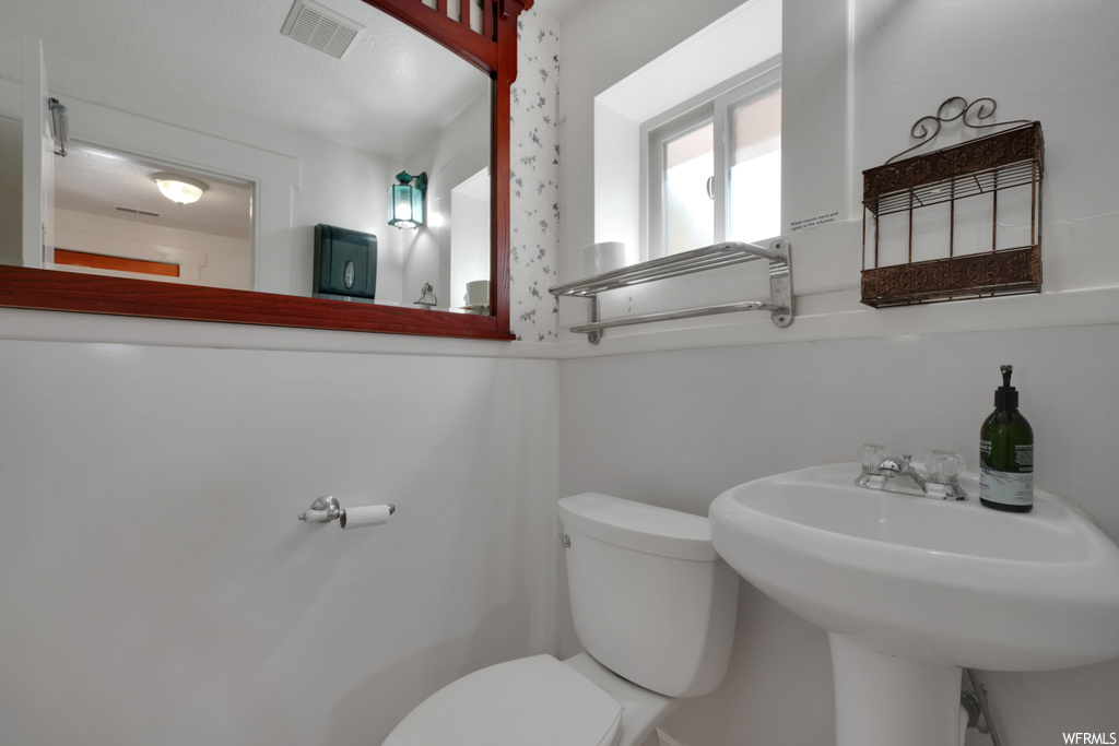 Half bathroom featuring natural light, toilet, mirror, and washbasin