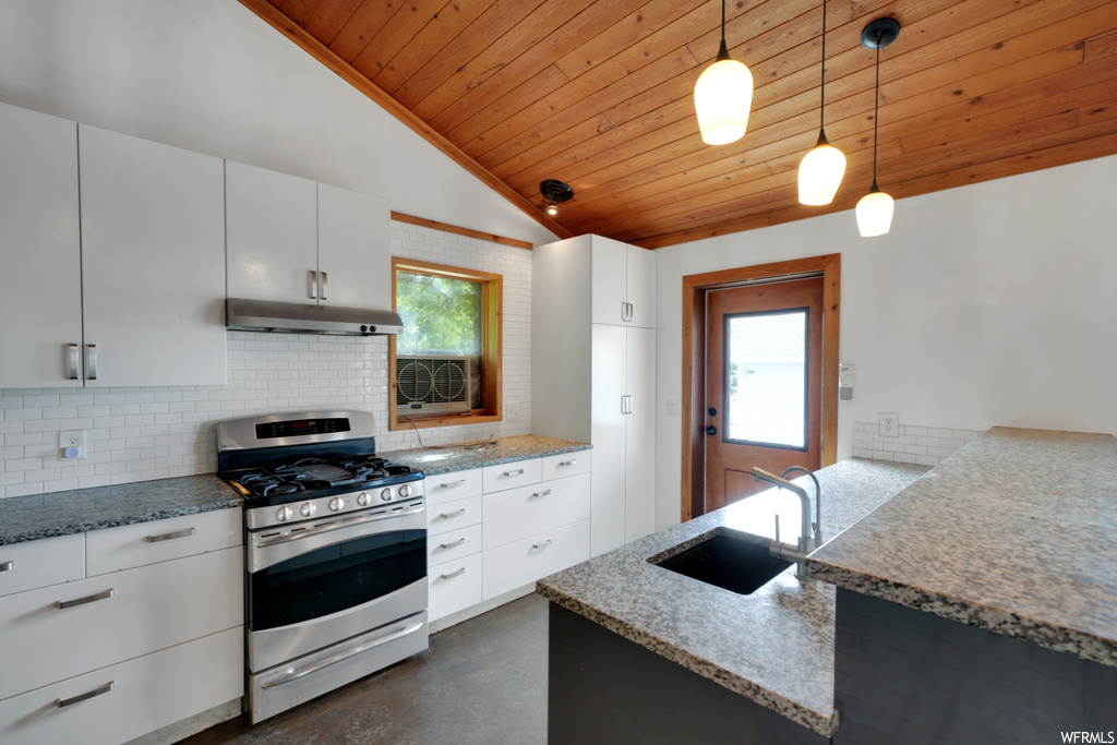 Kitchen featuring lofted ceiling, natural light, stainless steel finishes, gas range oven, range hood, white cabinets, pendant lighting, dark stone countertops, and dark floors