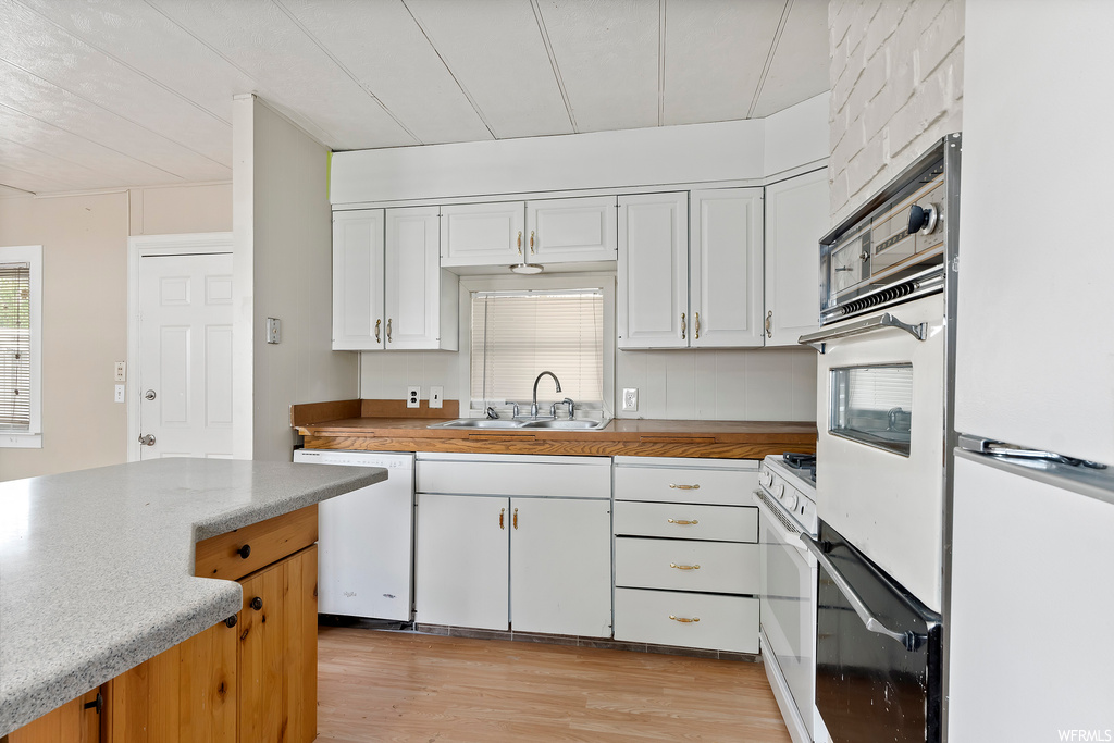 Kitchen featuring natural light, dishwasher, refrigerator, white cabinets, light countertops, and light hardwood floors