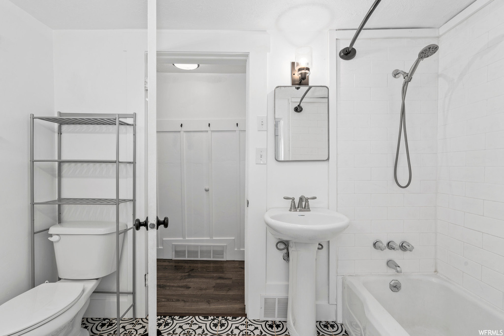 Full bathroom with hardwood floors, toilet, mirror, washtub / shower combination, and washbasin