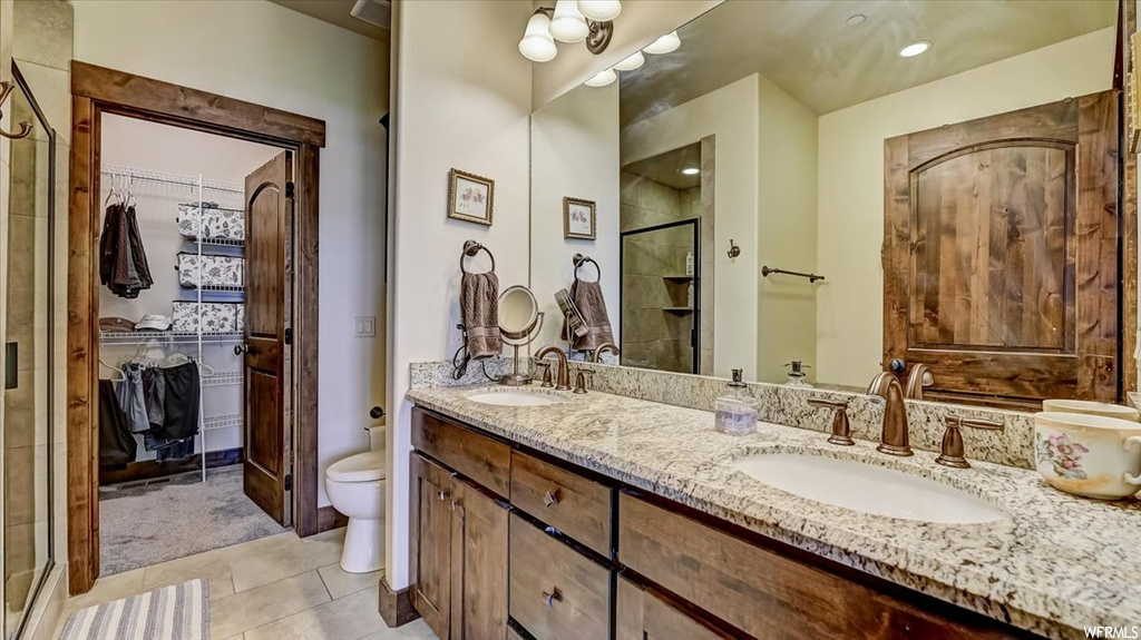 Bathroom with tile flooring, toilet, mirror, his and hers vanity, and shower door