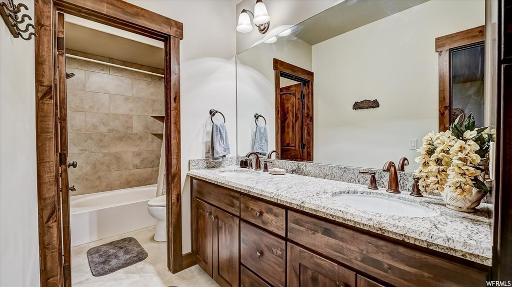 Full bathroom with tile floors, shower / bathtub combination, double sink vanity, mirror, toilet, and shower curtain