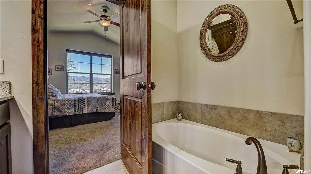 Bathroom with natural light, a ceiling fan, mirror, vanity, and a bathtub