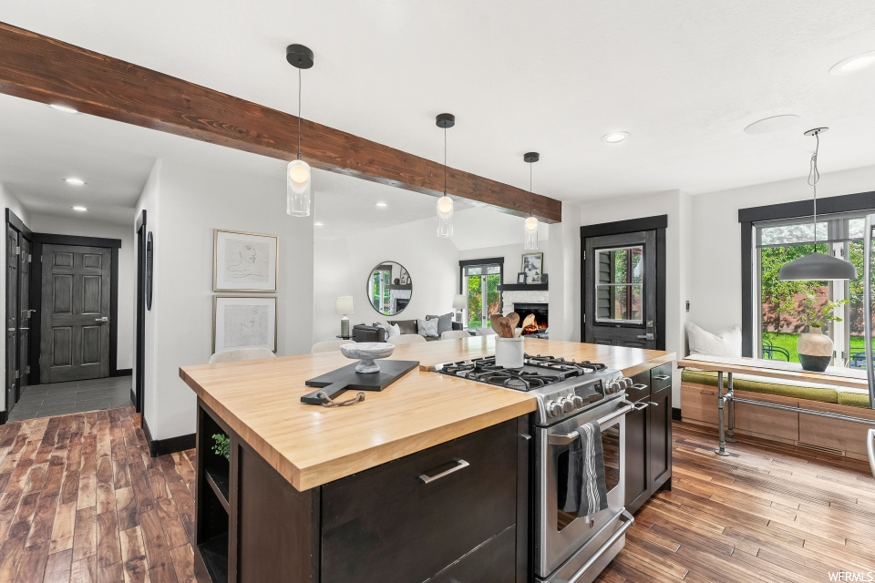 Kitchen with wood-type flooring, natural light, stainless steel finishes, gas range oven, pendant lighting, light countertops, and dark brown cabinetry