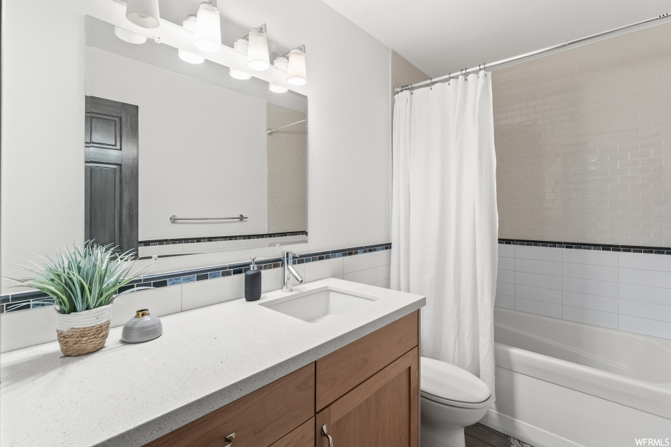 Full bathroom with bathtub / shower combination, mirror, toilet, vanity with extensive cabinet space, and shower curtain