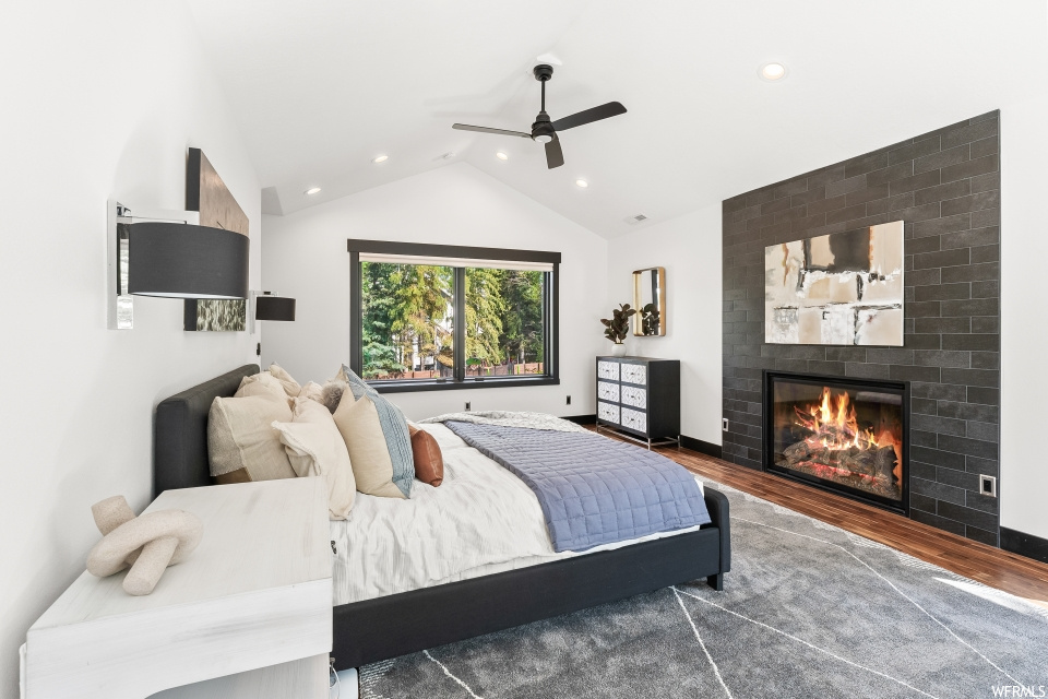 Hardwood floored bedroom featuring a fireplace, a ceiling fan, lofted ceiling, and natural light