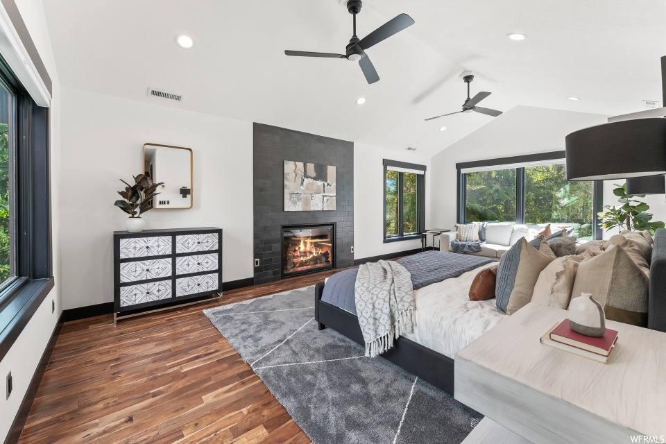Bedroom featuring a ceiling fan, lofted ceiling, hardwood floors, a fireplace, and natural light