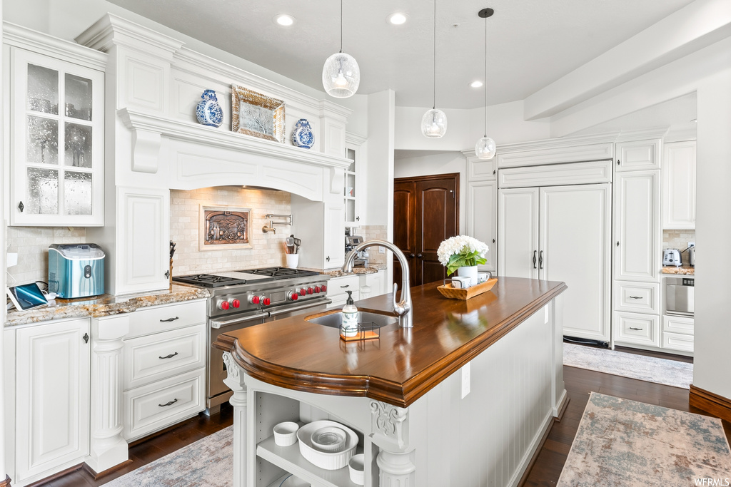 Kitchen featuring a center island, wood-type flooring, stainless steel finishes, gas range oven, dark granite-like countertops, and pendant lighting