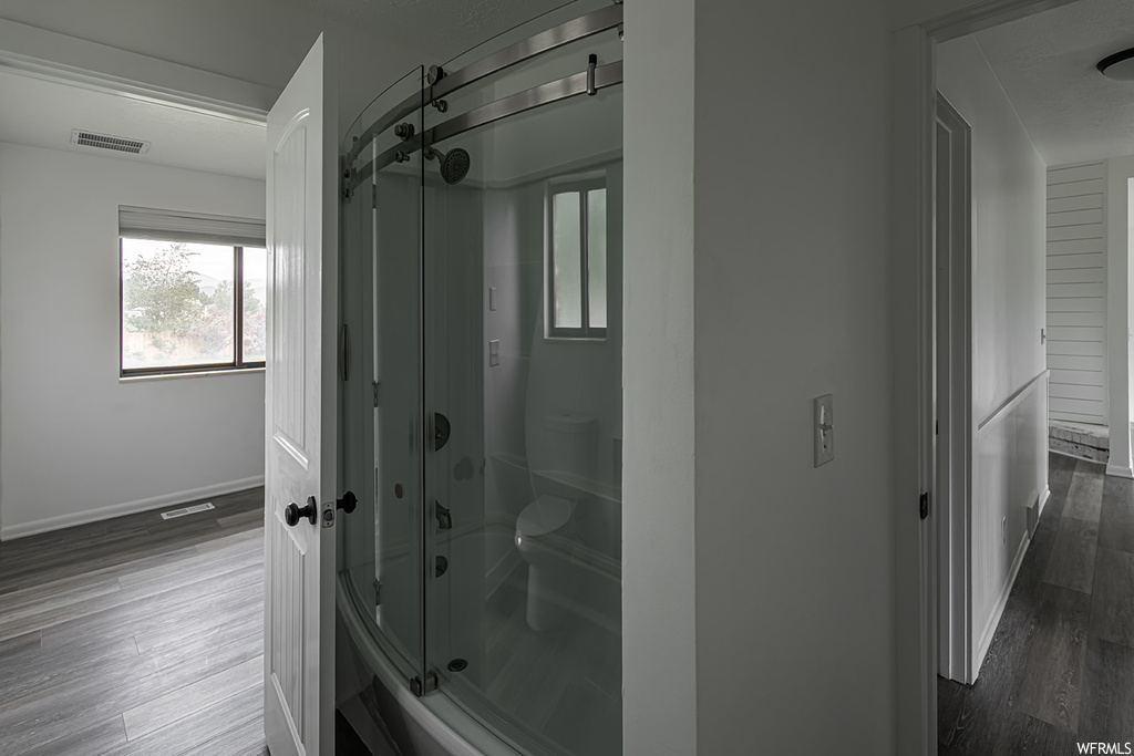 Bathroom featuring hardwood flooring, natural light, toilet, and shower door