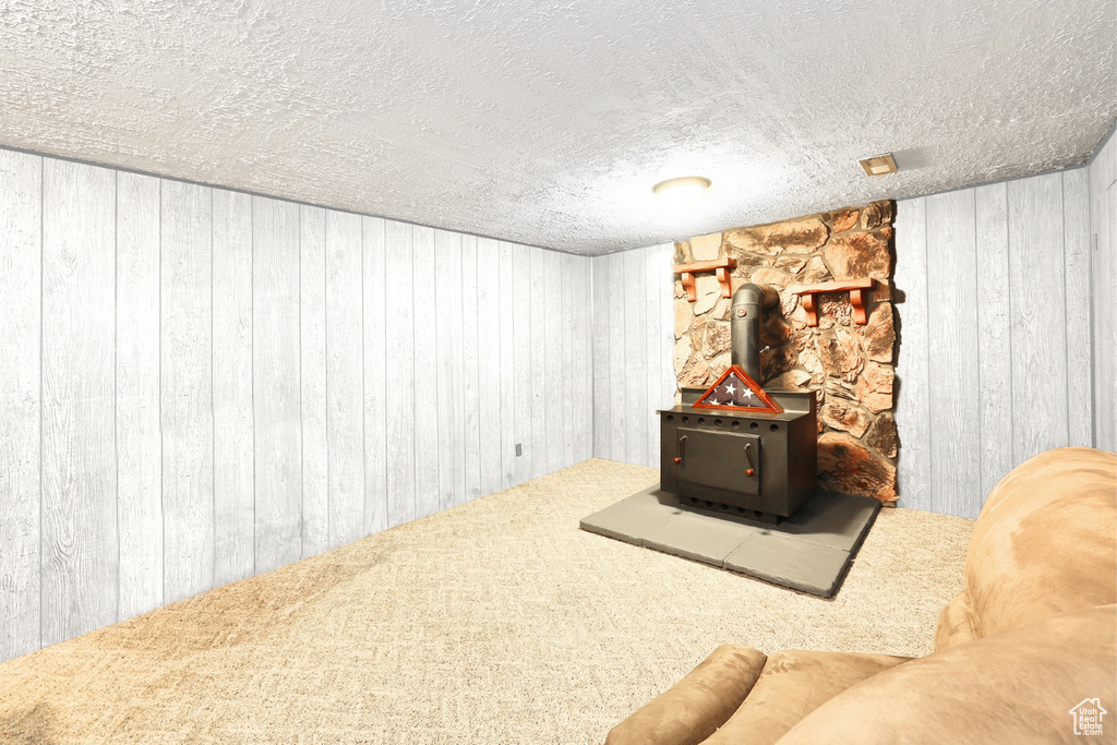 Unfurnished living room with carpet floors, wood walls, a wood stove, and a textured ceiling