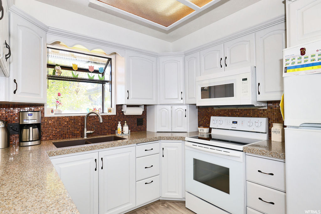 Kitchen with electric range oven, refrigerator, microwave, light stone countertops, and white cabinetry