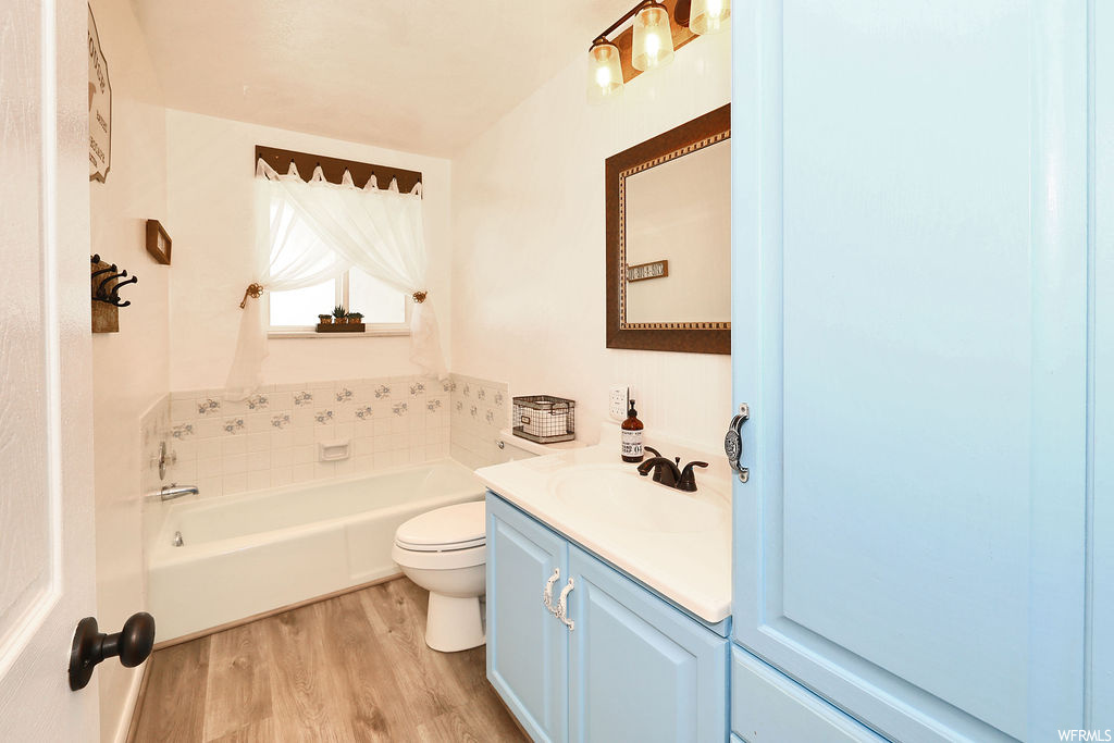 Bathroom featuring hardwood floors, toilet, mirror, large vanity, and a bathtub