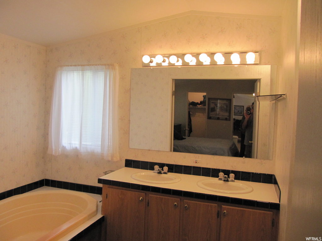 Bathroom featuring lofted ceiling, mirror, dual vanity, and a bathtub