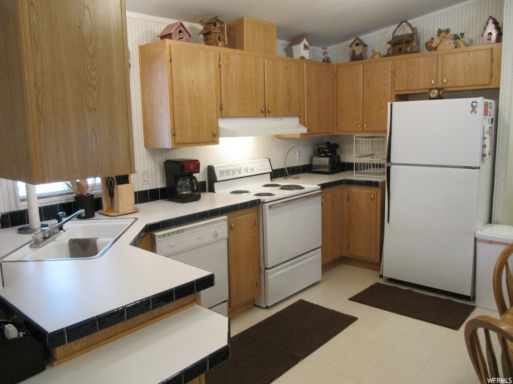 Kitchen with fume extractor, dishwasher, refrigerator, electric range oven, light tile flooring, and brown cabinets