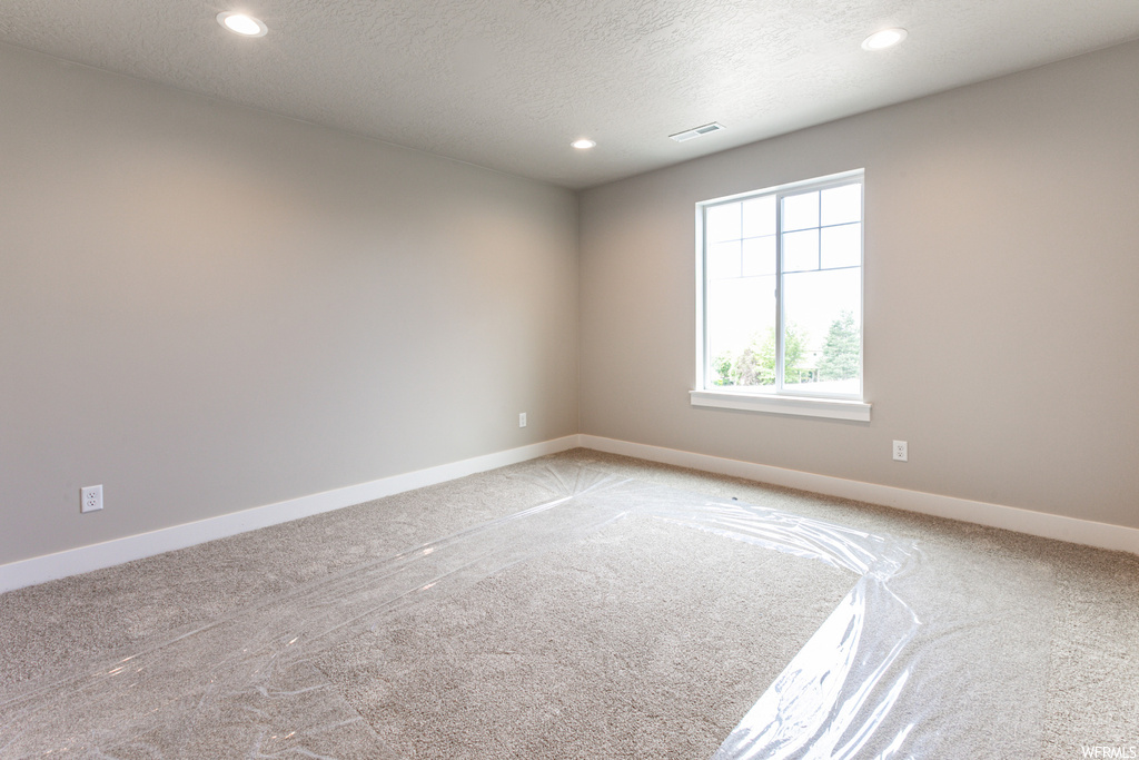 Empty room with a textured ceiling and light carpet
