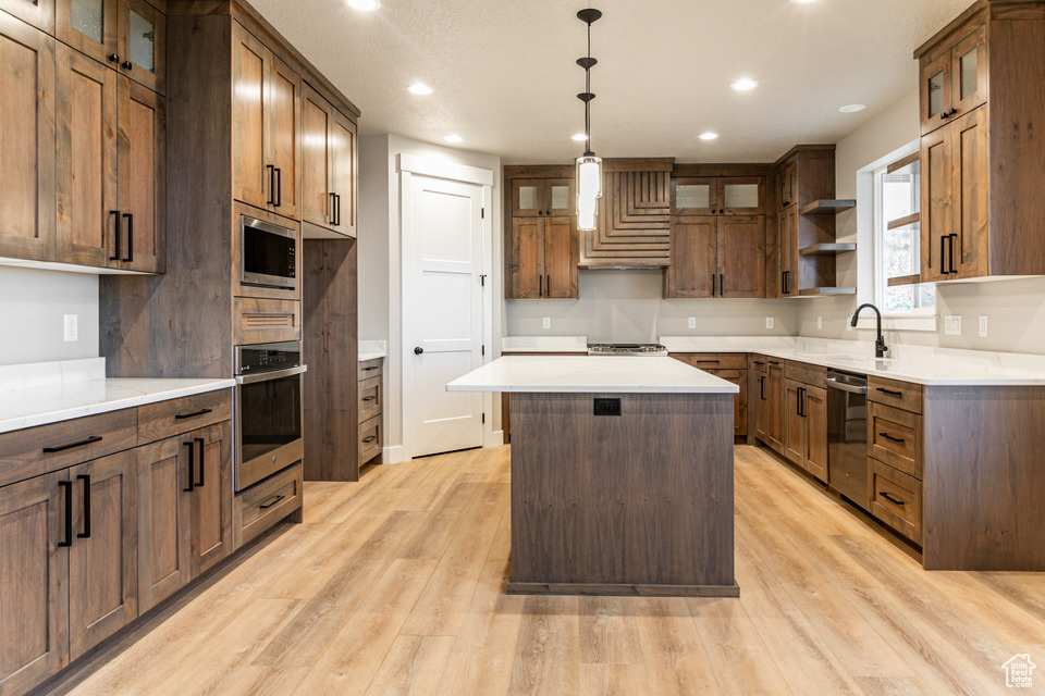 Kitchen with light hardwood / wood-style floors, stainless steel appliances, a center island, fume extractor, and hanging light fixtures